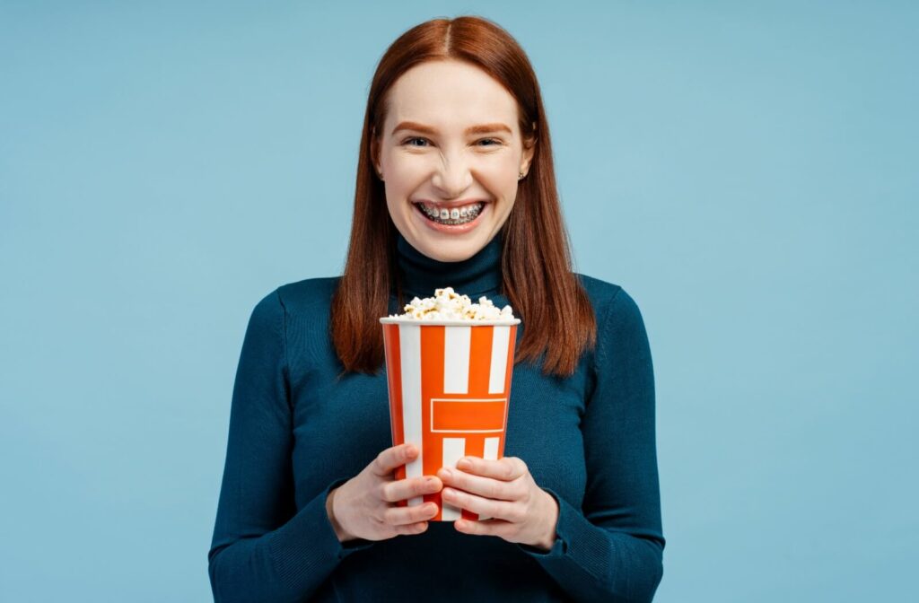 A woman with dental braces holding a bucket of popcorn.