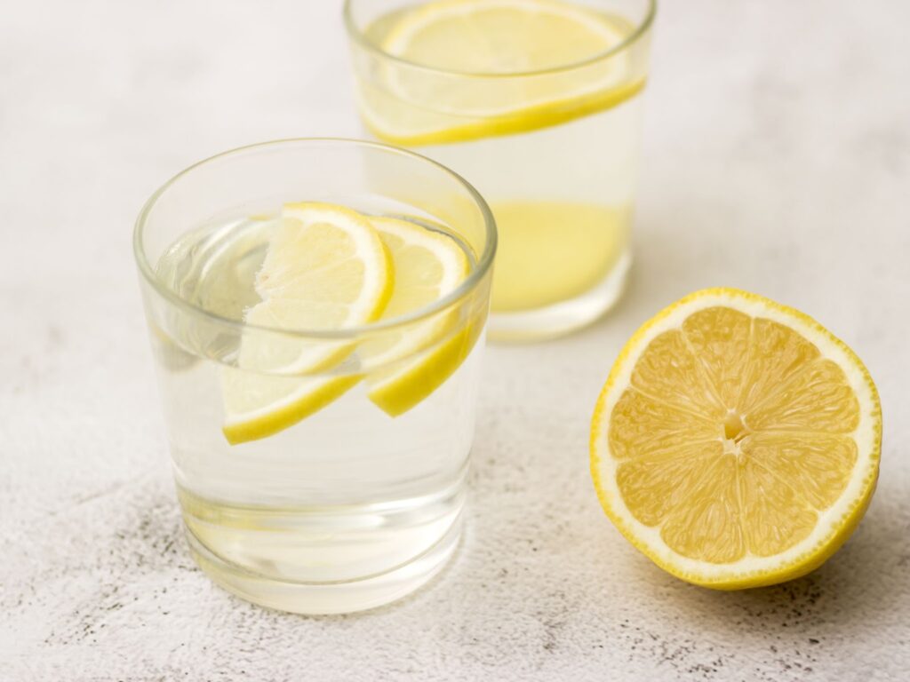 Close-up of two glasses of lemon water and half of a lemon on a countertop.