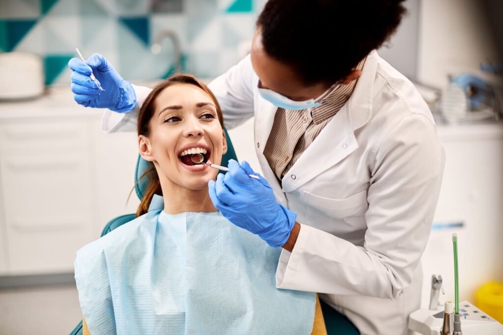 A dentist performing a dental exam on a young woman sitting in a dental chair.