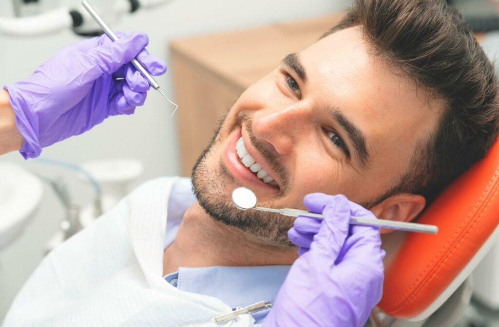 A young adult with veneers smiling after a dentist checks their teeth for cavities during a dental exam.