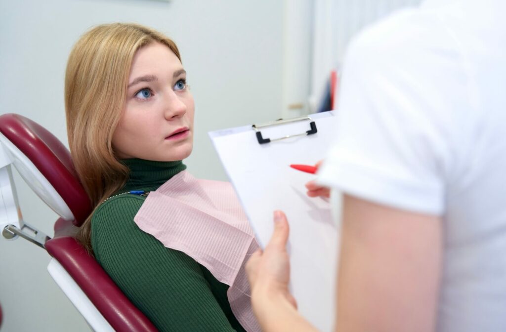 Patient in a dental chair discussing teeth cleaning and aftercare with a dentist holding a clipboard