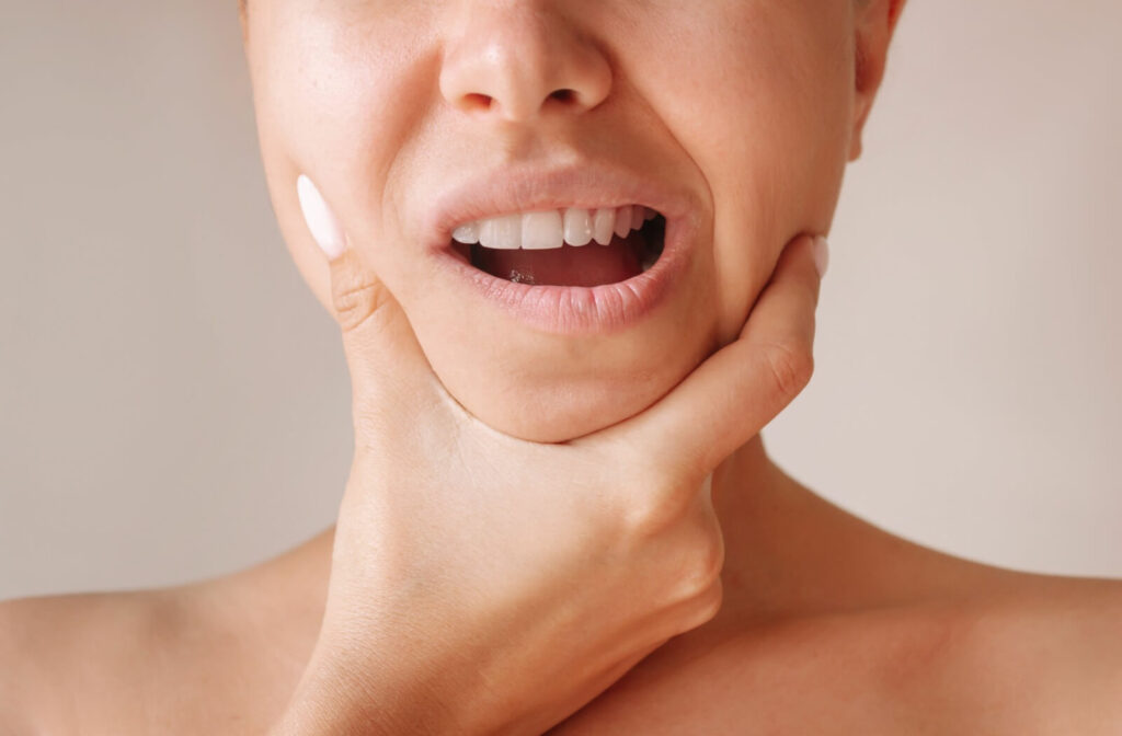 A person uses their hand to cup their jaw to relieve pain from TMJ.
