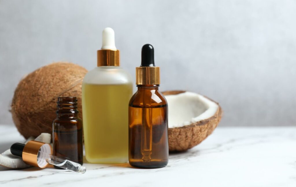 Pieces of a coconut sit on a white table. Several bottles of virgin coconut oil are placed in front of the coconut shell.