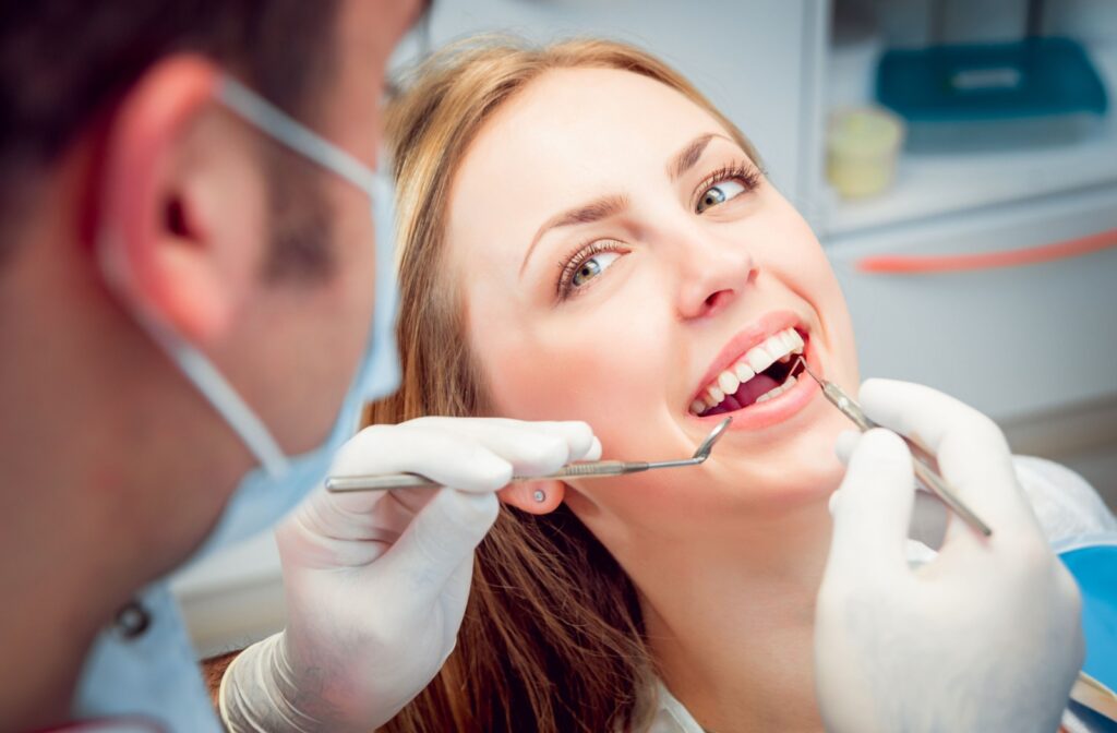 Smiling woman as a dentist examines her teeth for cavities with dental instruments in a clinic setting.