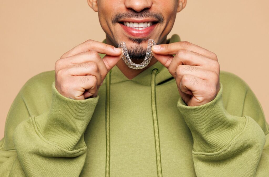 A person holding up an invisalign tray to their mouth and smiling